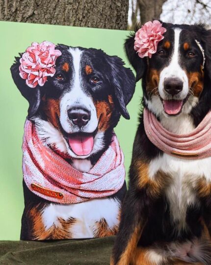 A large dog with a pink flower on its head and a pink scarf sits outdoors by a tree, next to the custom-pet-art-canvas-wrap-987844_1024x1024—a pop art portrait of itself in solid colors.