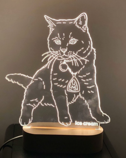 The Customized Pet Lamp Design features a glowing cat-shaped LED acrylic on a wooden base. In the dark room, its white outline and "ice cream" etching evoke pet canvas art for a unique, personalized touch.