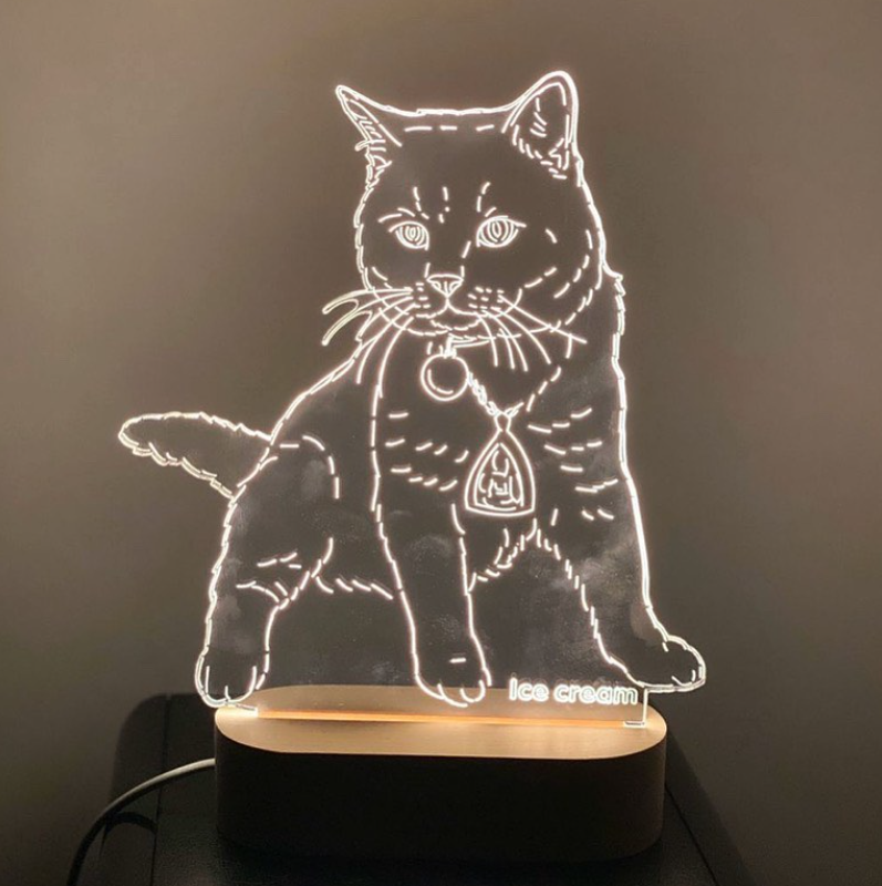 The Customized Pet Lamp Design features a glowing cat-shaped LED acrylic on a wooden base. In the dark room, its white outline and "ice cream" etching evoke pet canvas art for a unique, personalized touch.