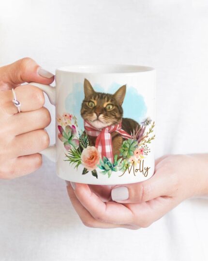 A person holds the Flower Wreath Custom Design Mug #1, featuring a tabby cat portrait with a pink bow, surrounded by colorful flowers and greenery in pet canvas style. The name Molly appears in script on the white mug.