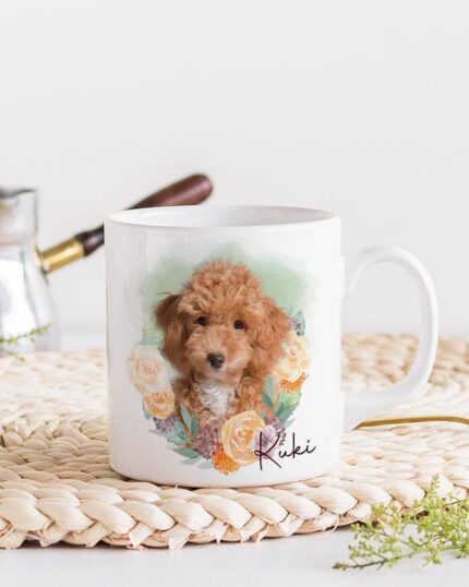 The Flower Wreath Custom Design Mug #1 displays a custom pet canvas painting of Luki, a brown, curly-haired dog among flowers. The white mug sits on a woven mat with a gold spoon, green leaves, and metal coffee maker nearby.