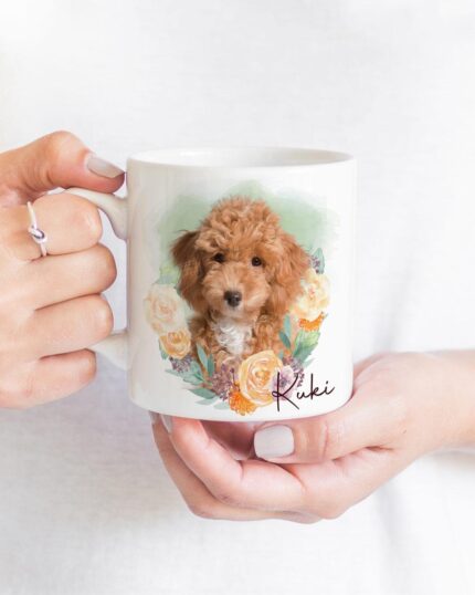 A person wearing a white shirt and a ring holds the Flower Wreath Custom Design Mug #1, which displays a custom pet illustration of a brown curly-haired dog named Kuki in cursive, surrounded by flowers.