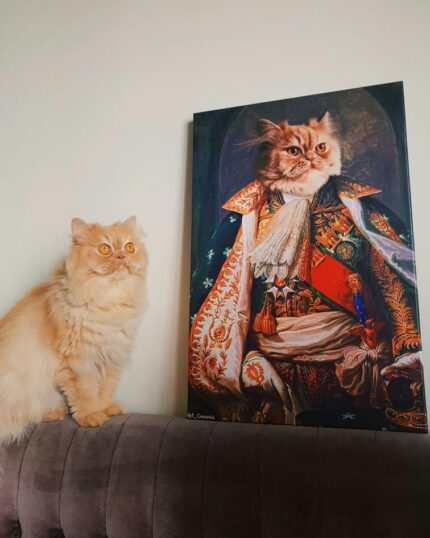 A fluffy orange cat sits on a couch beside a framed portrait—The King #3 - Custom Design Canvas Painting—depicting the cat dressed in elaborate royal attire, resembling a regal historical figure.