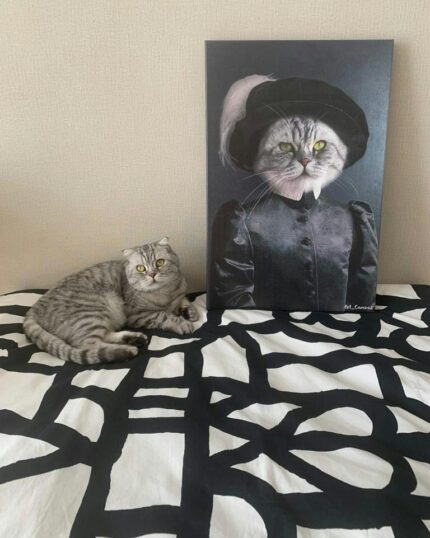 A gray tabby cat rests on a black-and-white bedspread beside The Noble Gentleman #7 - Custom Design Canvas Painting, which features the cat’s portrait in a black Renaissance-style outfit and hat, mirroring its real-life appearance.