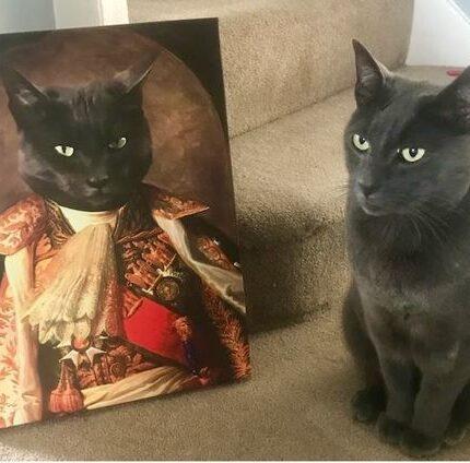 A grey cat sits on a carpeted staircase beside "The King #3 - Custom Design Canvas Painting," which features a regal cat in ornate attire. Both the real and painted cats have strikingly similar poses and expressions.
