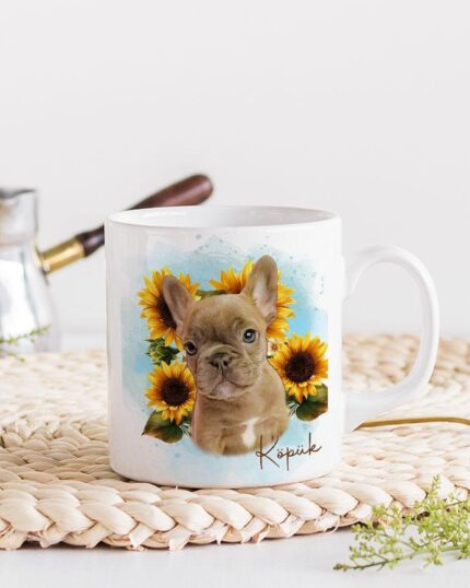 The Flower Wreath Custom Design Mug #1 features a white mug with a French Bulldog puppy among sunflowers on a woven placemat—perfect for fans of unique, personalized pet designs.