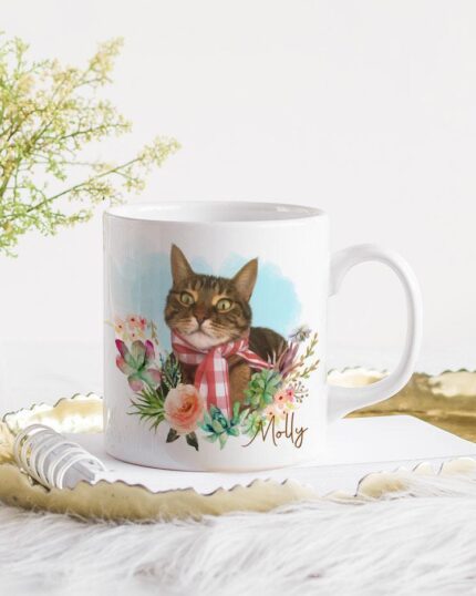 The Flower Wreath Custom Design Mug #1 features a tabby cat in a pink scarf, surrounded by flowers and the name Milly—perfect for custom pet art lovers and displayed beautifully on a gold tray with greenery.