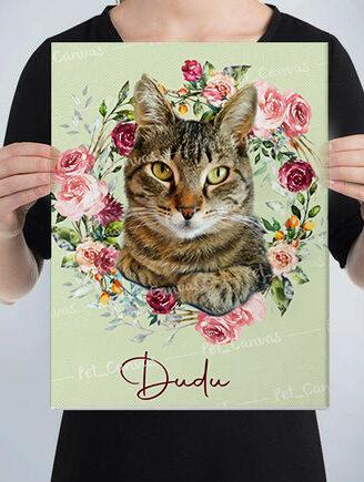 A person holds a custom design pet canvas featuring a tabby cat surrounded by a colorful floral wreath, with the name Dudu written in cursive at the bottom of the image.