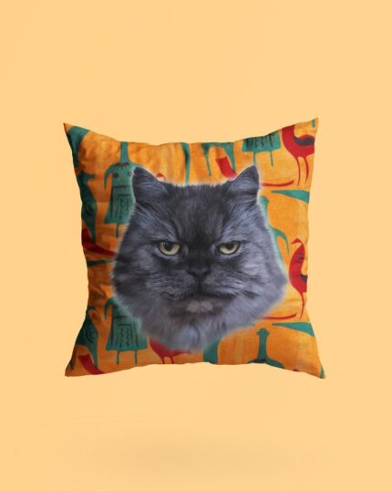 The Personalized Pop Art Pillow – Donut features a realistic grumpy gray cat face on a vibrant orange background with abstract animal shapes, printed on canvas and set against a plain light peach backdrop.