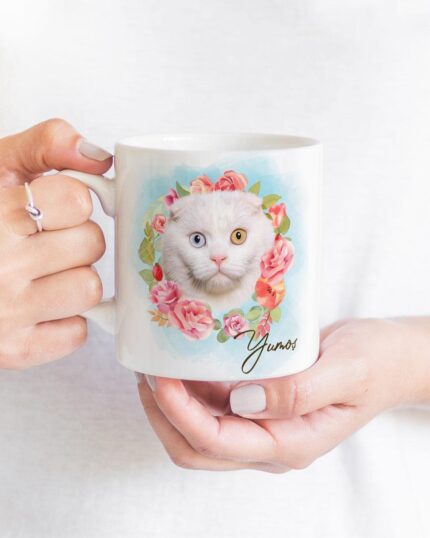 A person holds the Flower Wreath Custom Design Mug– no#7, featuring a custom pet canvas illustration of a white cat with heterochromia, surrounded by pink flowers and green leaves, with the name Yunos on the mug.