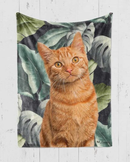 A realistic illustration of an orange tabby cat with large green leaves is featured on the Custom Design Pop-Art Blanket – Leaf #1, displayed hanging against a white wooden wall.