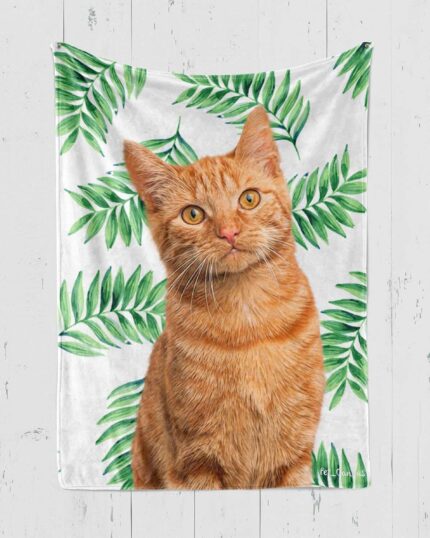 The Personalized Pop-Art Blanket – Leaf Collection showcases a realistic orange tabby cat against green leafy patterns, beautifully displayed on a white wooden wall.