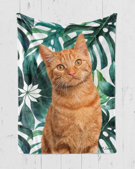 A realistic orange tabby cat sits before a white towel with bold green tropical leaves on a white wood backdrop, offering perfect inspiration for your Personalized Pop-Art Blanket – Leaf Collection.
