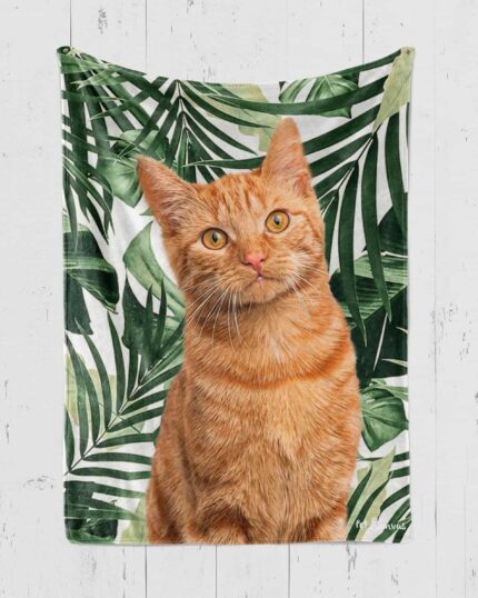 The Personalized Pop-Art Blanket – Leaf Collection features a custom design of an orange tabby cat among lush green tropical leaves, beautifully showcased against a white wooden wall.