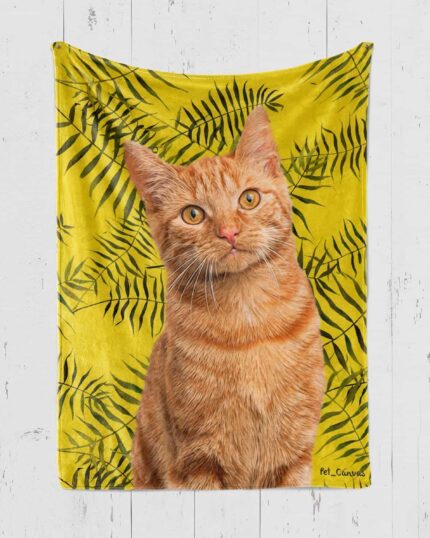 A lifelike illustration of an orange tabby cat is featured on the Personalized Pop-Art Blanket – Leaf Collection, set against a bright yellow background with black fern leaves, hanging on a white wooden wall.