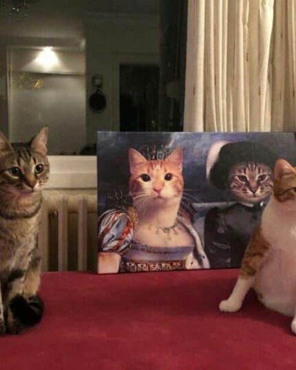 Two cats sit on a red surface before a painting humorously depicting them as royalty. The "Multiple Portraits #9 Queen and Noble Bey" custom pet canvas adds charm with its window, curtain backdrop, and warm indoor lighting.
