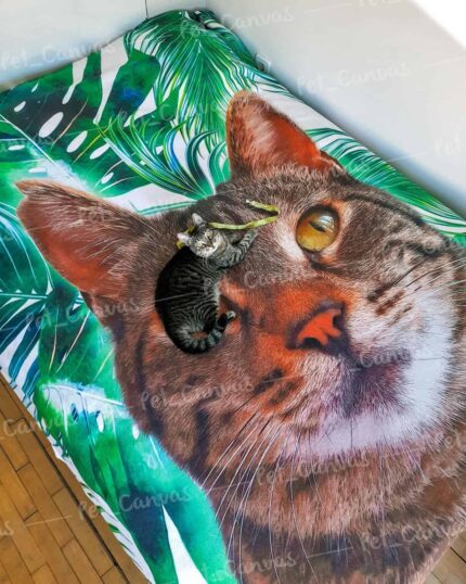 A small gray tabby kitten is curled up on the Custom Design Pop-Art Blanket – Leaf #3, featuring a large, realistic cat face and green leafy patterns. The kitten lies right on top of the larger cat’s nose in the design.