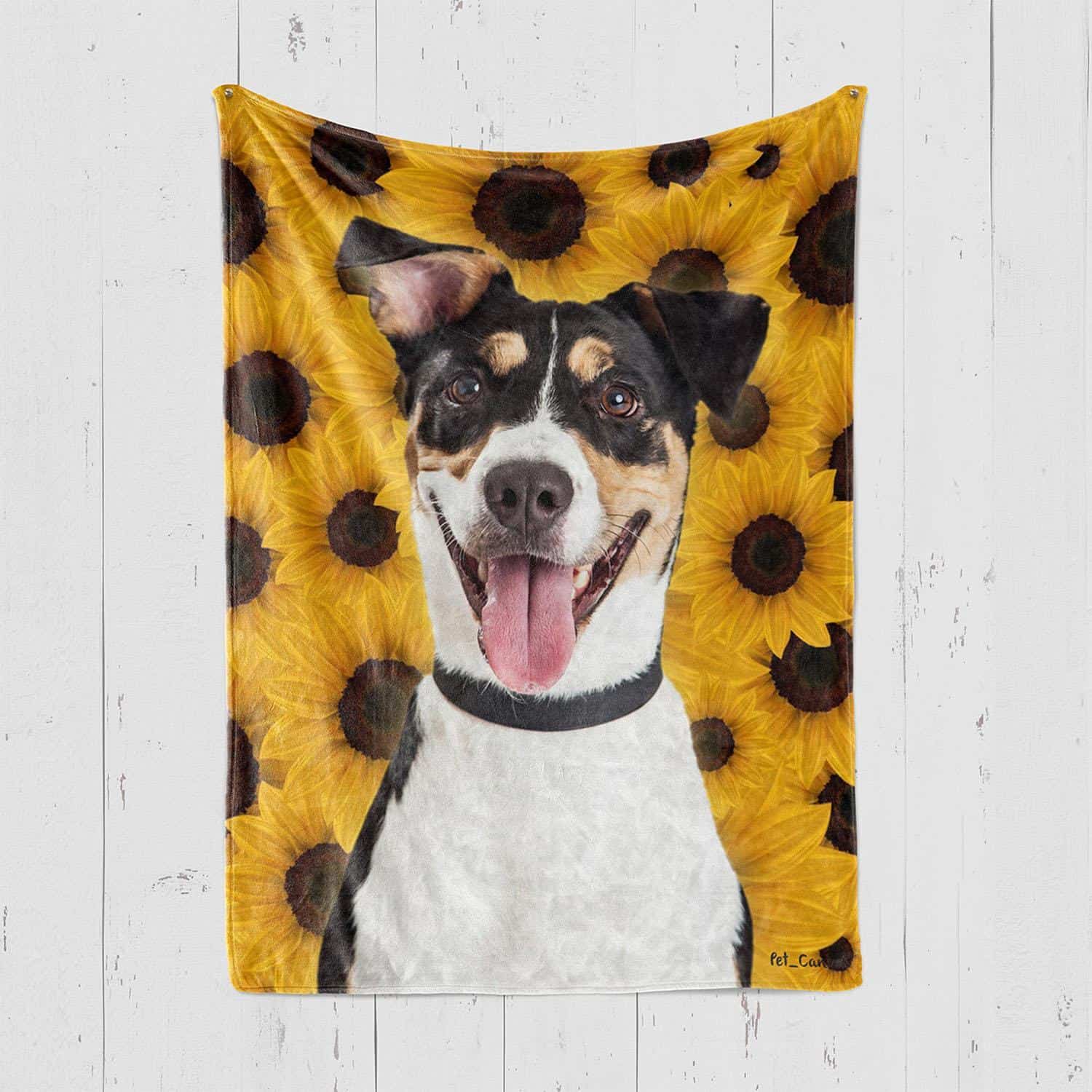 A Cheerful Black, White, And Tan Dog With Its Tongue Out Is Pictured On The Custom Design Pop-Art Blanket – Sunflower, Featuring A Bright Yellow Sunflower Pattern And Displayed On A White Wooden Wall. A cheerful black, white, and tan dog with its tongue out is pictured on the Custom Design Pop-Art Blanket – Sunflower, featuring a bright yellow sunflower pattern and displayed on a white wooden wall.