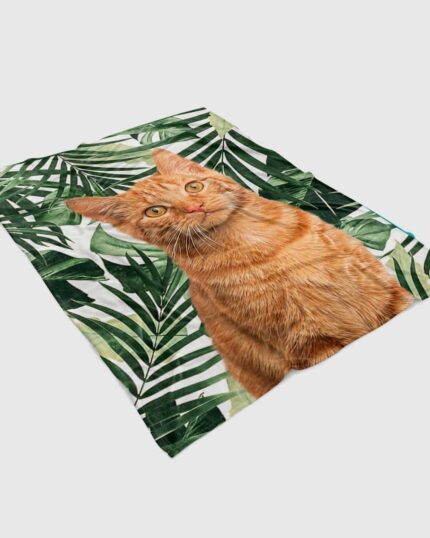 The Custom Design Pop-Art Blanket – Leaf #5 features a lifelike orange tabby cat sitting before a green tropical leaf pattern, inspired by custom pet canvas art for a unique and cozy accent.