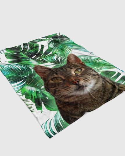 The Custom Design Pop-Art Blanket – Leaf #3 showcases a bold tabby cat face among green tropical leaves on white—ideal for fans of unique pet decor and custom home accessories.