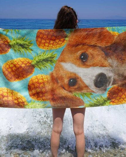 A person stands at the ocean’s edge with the Custom Design 3D Printed Beach Towel – Pineapple, featuring a vibrant dog face and pineapple print on blue canvas as waves splash around their legs.