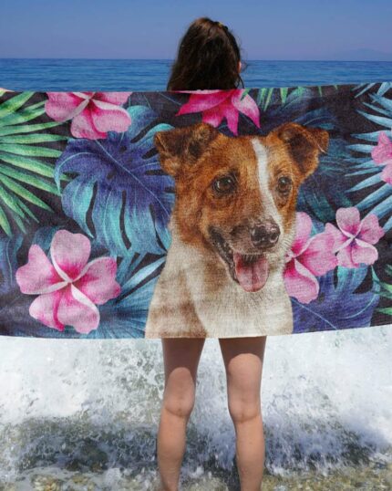 Bir kişi, Özel Tasarım 3D Baskılı Plaj Havlusu – Tropikal Yapraklar'ı elinde tutarak kıyıda duruyor. Mavi okyanus berrak gökyüzünün altında uzanırken, dalgalar ayaklarının dibinde kırılıyor.