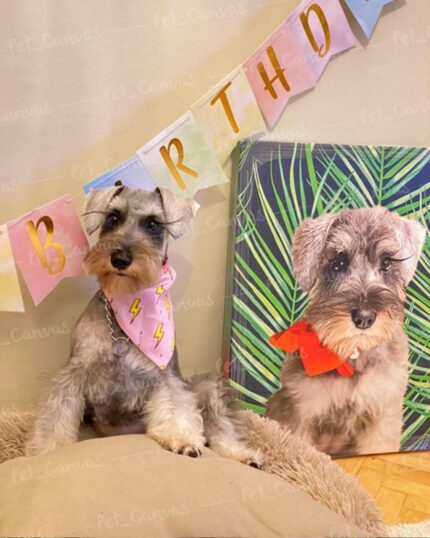 A small gray dog with a pink bandana sits on a dog bed before a pastel BIRTHDAY banner and a custom Pop Art – Leaf #4 pet canvas showing the same dog in a red bow, all against a green leafy backdrop.