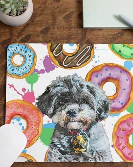 The Custom Pet Art Mouse Pad features donuts and a cute black-and-gray dog in a bow tie, inspired by custom pet canvas art. Shown on a wooden desk with keyboard, mouse, notebook, pen, and potted plant.