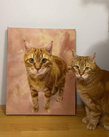 A ginger tabby cat sits on a wooden floor beside the Masterpiece Portrait - Multicolor canvas featuring its portrait. The custom background color of the canvas matches the wall and floor, with both cat and portrait facing the camera.