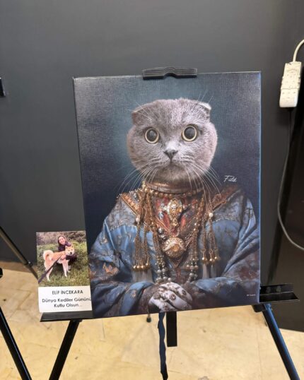 A Majestic Mouser - Aristocratic Pet Portrait featuring a gray cat in royal attire with jewelry is displayed on an easel. Beside it are a woman holding her cat and a card reading "Dünya Kediler Gününüz Kutlu Olsun.