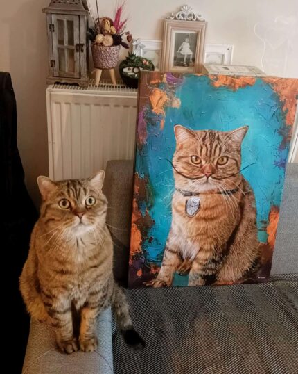 A tabby cat with green eyes sits on a gray couch beside a Salvador Dali Style – Custom Design Pet Canvas featuring its portrait against a blue backdrop, both mirroring each other's pose and expression.