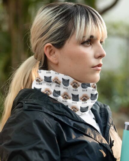 A woman with blond and black hair in a ponytail wears a Custom Neck Gaiter With Pet Faces featuring “Luna” and “Lucy.” She’s outdoors in a black jacket, holding a blue tumbler, showcasing the custom pet-themed accessory.