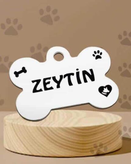 A white Custom Pet Tag, bone-shaped with ZEYTİN in bold black letters, decorated with paw print, bone, and heart icons—ideal for pet lovers—displayed on a wooden platform against a brown paw print background.