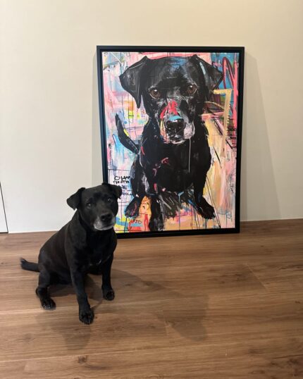 A black dog with a white muzzle sits on a wooden floor in front of a Custom Design Abstract Pet Portrait canvas featuring its image, set against a plain beige wall.