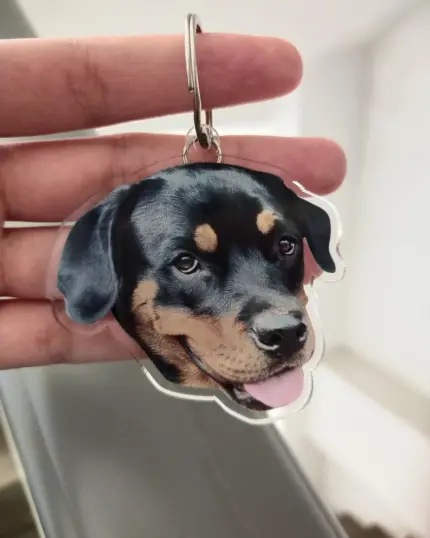 A hand holds a Personalized Animal Printed Plexiglass Keychain featuring a lifelike Rottweiler face with its mouth open and tongue out, while the blurred background highlights the custom design and quality print of the keychain.