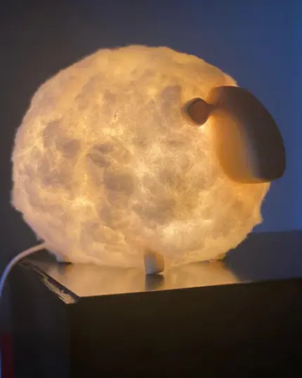 The Soft Cotton Sheep Night Light, featuring a glowing cloud-like body and smooth oval face, sits on a dark surface in a dim room—perfect to pair with your favorite custom design pet canvas.