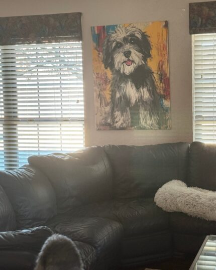 A cozy living room features a black sectional sofa, fluffy white pillow, sunny windows with blinds, and a Custom Design Abstract Pet Portrait of a shaggy black-and-white dog displayed on the wall.