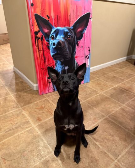 A black dog with large ears sits on a tiled floor in front of a Custom Design Abstract Pet Portrait showcasing its likeness on a vibrant red and blue background.