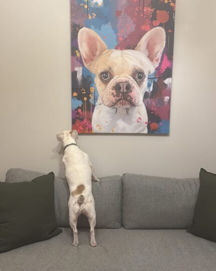 A small white dog with brown spots stands on a gray couch with two dark green cushions, looking at a Custom Design Abstract Pet Portrait of a similar dog hanging on the wall above.